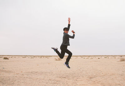 Full length of man jumping on beach against clear sky