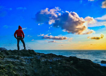 Rear view of man standing on rock by sea against sky