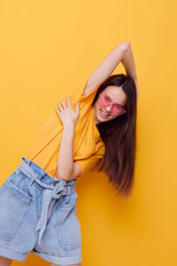 Portrait of young woman standing against yellow background