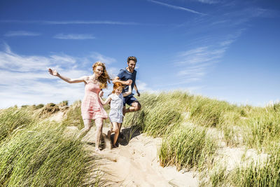 Netherlands, zandvoort, happy family with daughter running in beach dunes