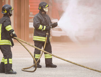 Firefighters spraying water from hose while standing on road