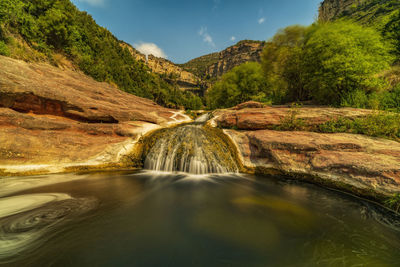 Scenic view of waterfall amidst trees against sky