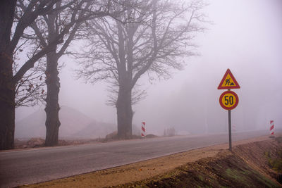 Road sign by bare trees during foggy weather