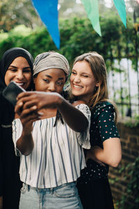 Happy multi-ethnic female friends taking selfie through mobile phone in backyard