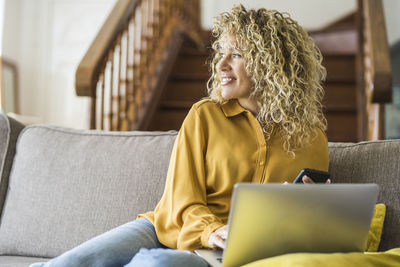 Young woman using laptop while sitting on sofa at home