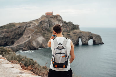 Rear view of man standing on rock by sea against sky