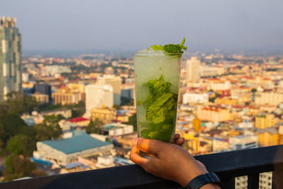 Cropped image of person holding drink against cityscape