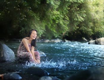 Full length of young woman standing on rock by river