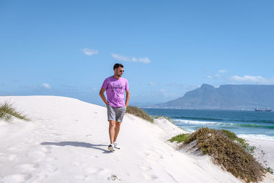 Rear view of man standing at beach against sky