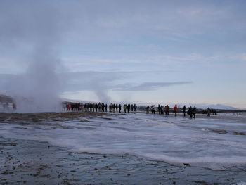 People watching steam on frozen landscape against sky