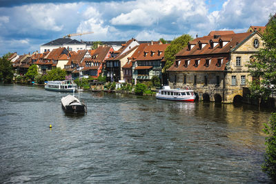 Sailboats in river by houses against sky in city