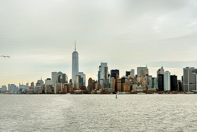 Sea by modern buildings in city against sky