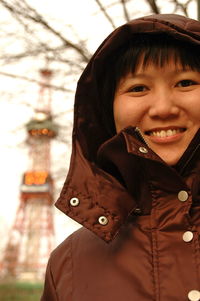 Portrait of smiling teenage girl wearing hood against sapporo tv tower at odori park