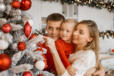 A mom, dad and young son decorate a christmas tree