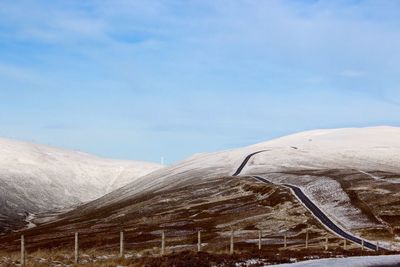 Scenic view of road across snowy mountains lagainst sky