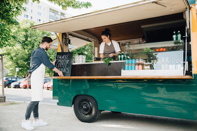 Male owner adjusting board on concession stand while partner working in food truck