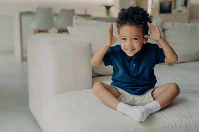 Portrait of cute boy sitting on bed at home