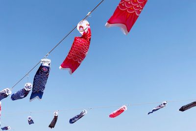 Low angle view of wind socks hanging against clear blue sky