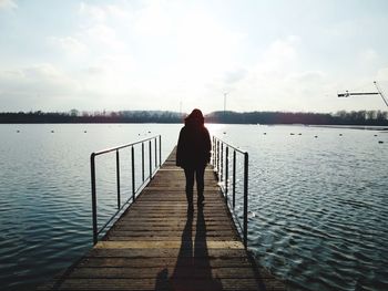 Rear view of woman walking on pier over lake against sky