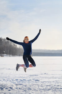 Excited woman with arms outstretched jumping on snow