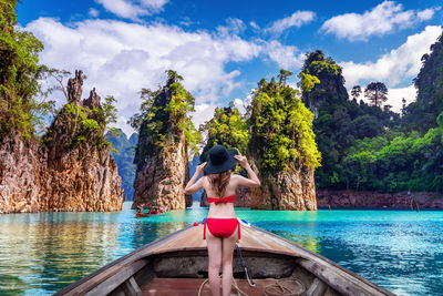 Rear view of woman standing by swimming pool against sky