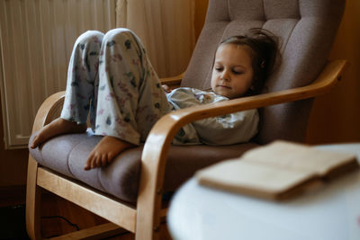 Bored sad toddler child lonely at home sitting on armchair. sad relaxed candid kid at home in cozy