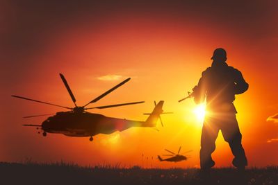 Silhouette army soldier standing on field against sky during sunset