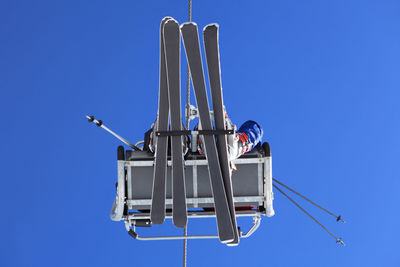 Directly below of people traveling in ski lift against clear blue sky