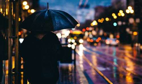 Rear view of man standing at night during rainy season