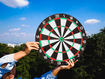 Close-up of woman holding dartboard against sky