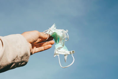 Close-up of hand holding mask against blue sky