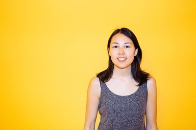 Portrait of smiling young woman against yellow background