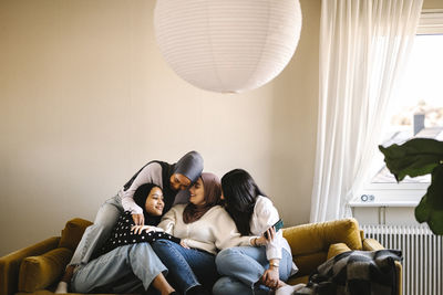 Smiling young woman embracing each other sitting on sofa in living room at home