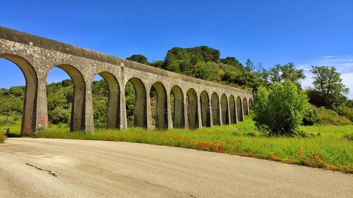 Arch bridge on field against blue sky