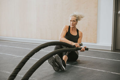 Mature woman exercising with battle rope at gym