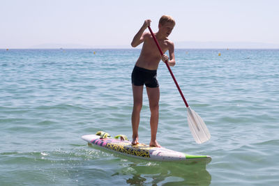 Shirtless teenage boy paddleboarding on sea