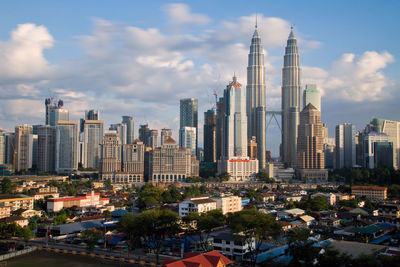 Petronas towers and buildings in city against cloudy sky