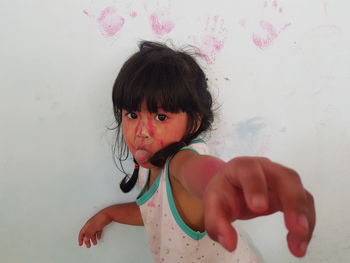Portrait of messy girl sticking out tongue against wall during holi