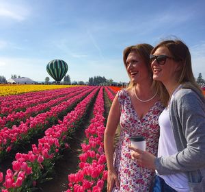 Smiling mother and daughter standing by flowering tulips against sky