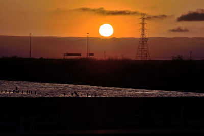 Silhouette electricity pylon against sky during sunset