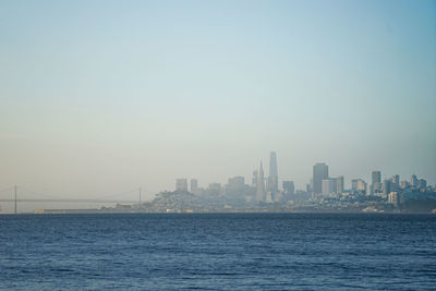 Sea and buildings in city against clear sky