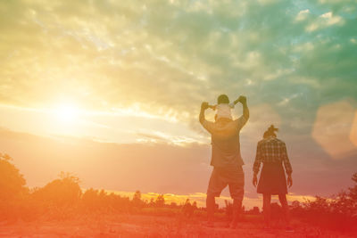 Rear view of women standing on field against sky during sunset