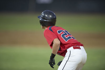 Looking over the shoulder of teen baseball runner leading off base