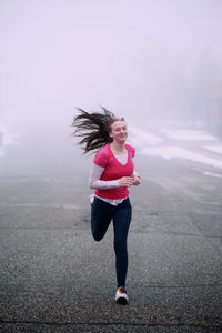 Full length of young woman running on road against sky