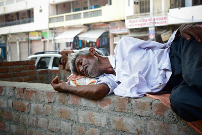 Senior homeless man relaxing on brick wall