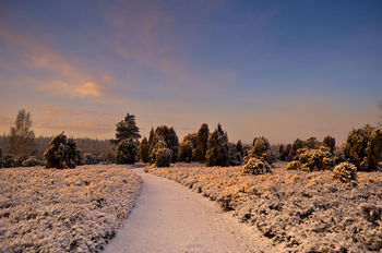 Snow covered landscape against sky during sunset