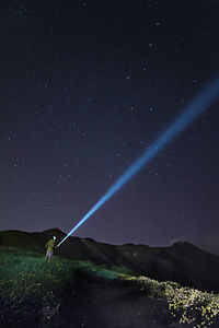 Man with flashlight standing on field against sky at night