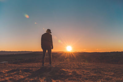 Rear view of man standing on field against sunset sky