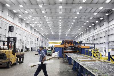 Side view of worker carrying wood while walking in steel industry factory