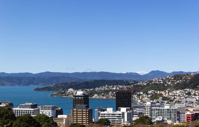 Buildings by sea against clear blue sky